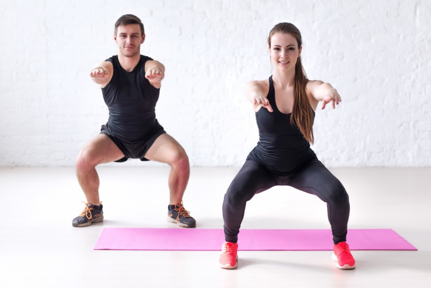 Fitness man and woman exercising squat exercise hands behind head looking at camera concept sport, training, warming up and lifestyle.